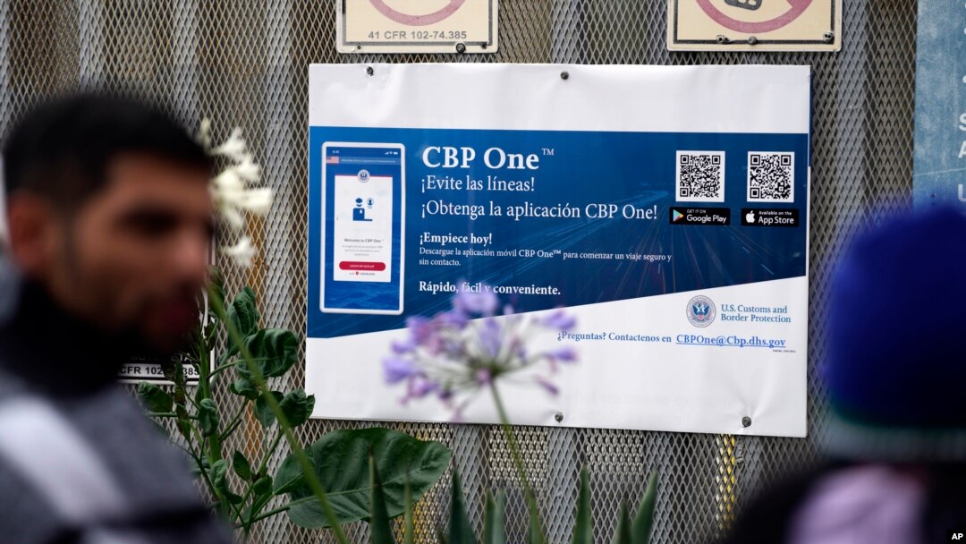 Varios solicitantes de asilo frente a un cartel que anuncia la app CBP One en el cruce fronterizo de San Isidro, que enlaza la ciudad de Tijuana, en México, con San Diego, en EEUU, el 1 de junio de 2023.