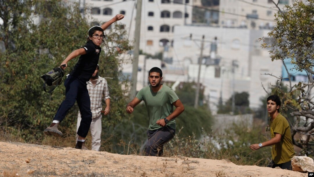 Muchachos israelíes lanzan piedras durante choques contra palestinos en las afueras del asentamiento judío de Kiryat Arba.