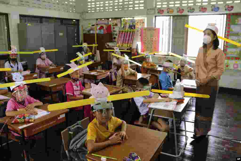 A teacher and students wearing hats designed for space keeper, practice social distancing to help curb the spread of the coronavirus at Ban Pa Muad School in Chiang Mai, north of Thailand.